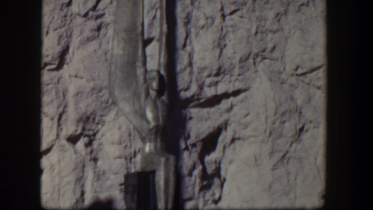 1954 Nevada 8mm frame showing an Egyptian-style vertical sculpture set against a textured stone wall.