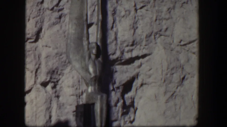 1954 Nevada 8mm frame showing an Egyptian-style vertical sculpture set against a textured stone wall.