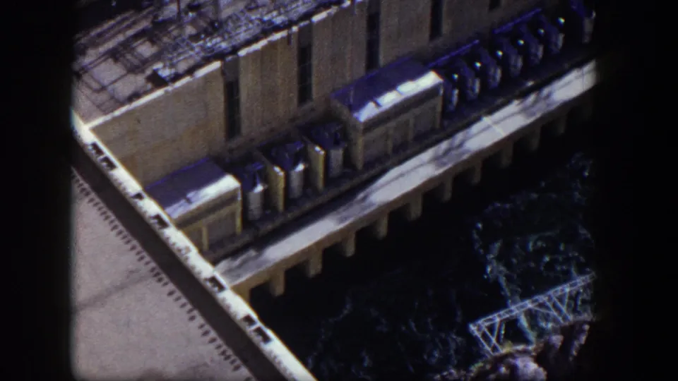 1954 Nevada 8mm frame showing an elevated view of a large concrete dam facility with water and railings below.