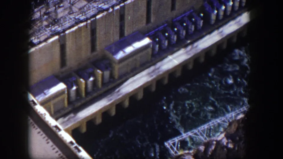 1954 Nevada 8mm frame showing a second elevated view of the dam facility, concrete deck, railings, and dark water below.