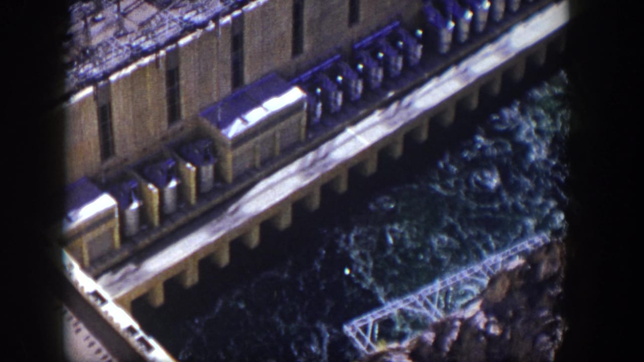 High-angle view of a concrete dam edge with churning blue-green water below.