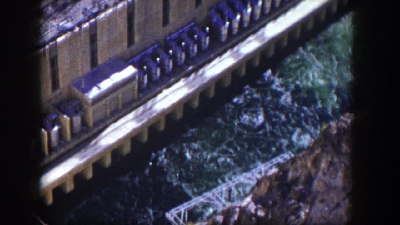 Concrete dam wall and spillway with foaming water seen from above.