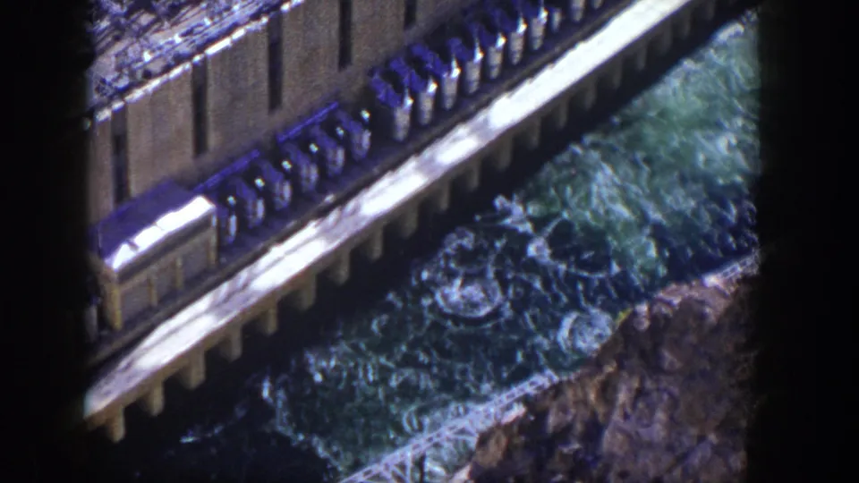 1954 Nevada 8mm frame with dark gate shadow, dam structure, and turbulent water flowing below the spillway.