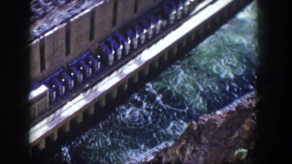 High-angle 1954 Nevada home-movie frame showing dam spillway water, concrete supports, and a lower truss structure.