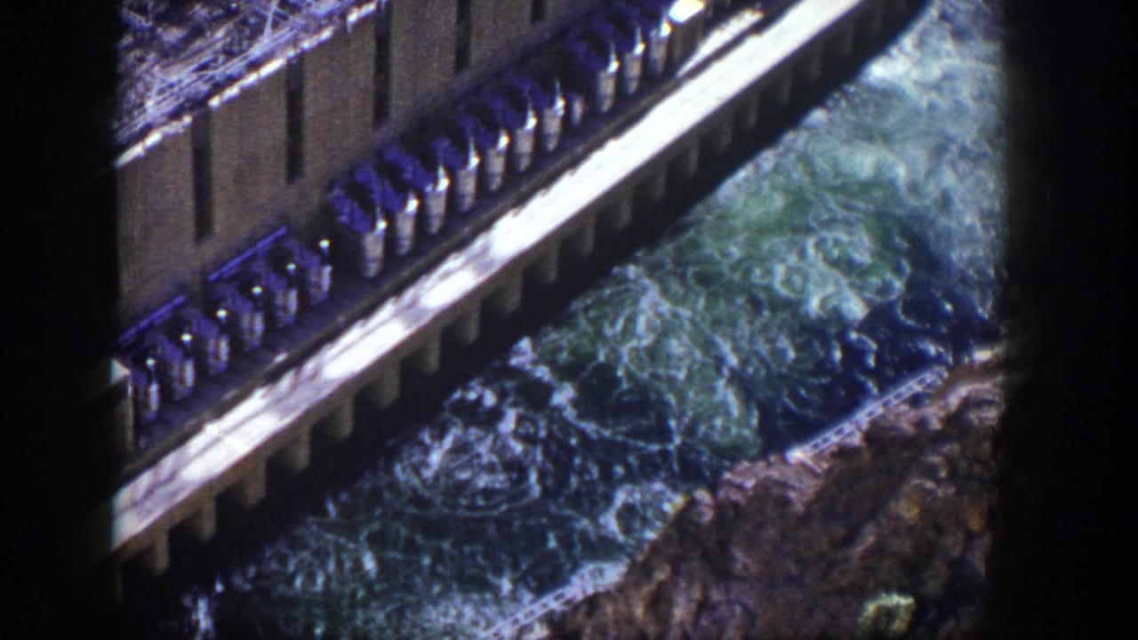 1954 Nevada 8mm frame showing a dam edge and foaming water rushing through a rocky channel below.