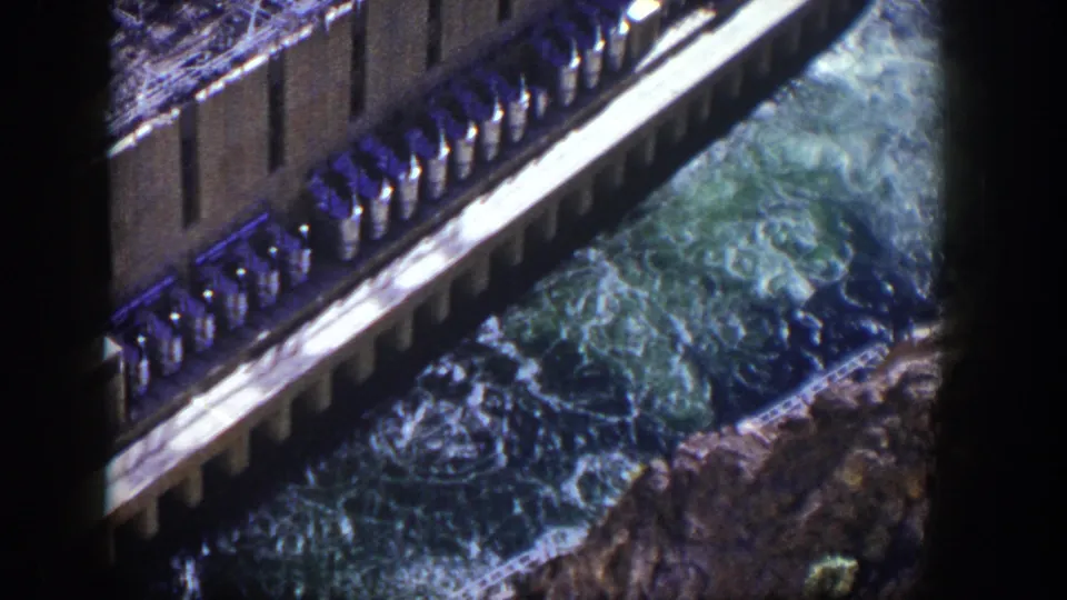 1954 Nevada 8mm frame showing a dam edge and foaming water rushing through a rocky channel below.