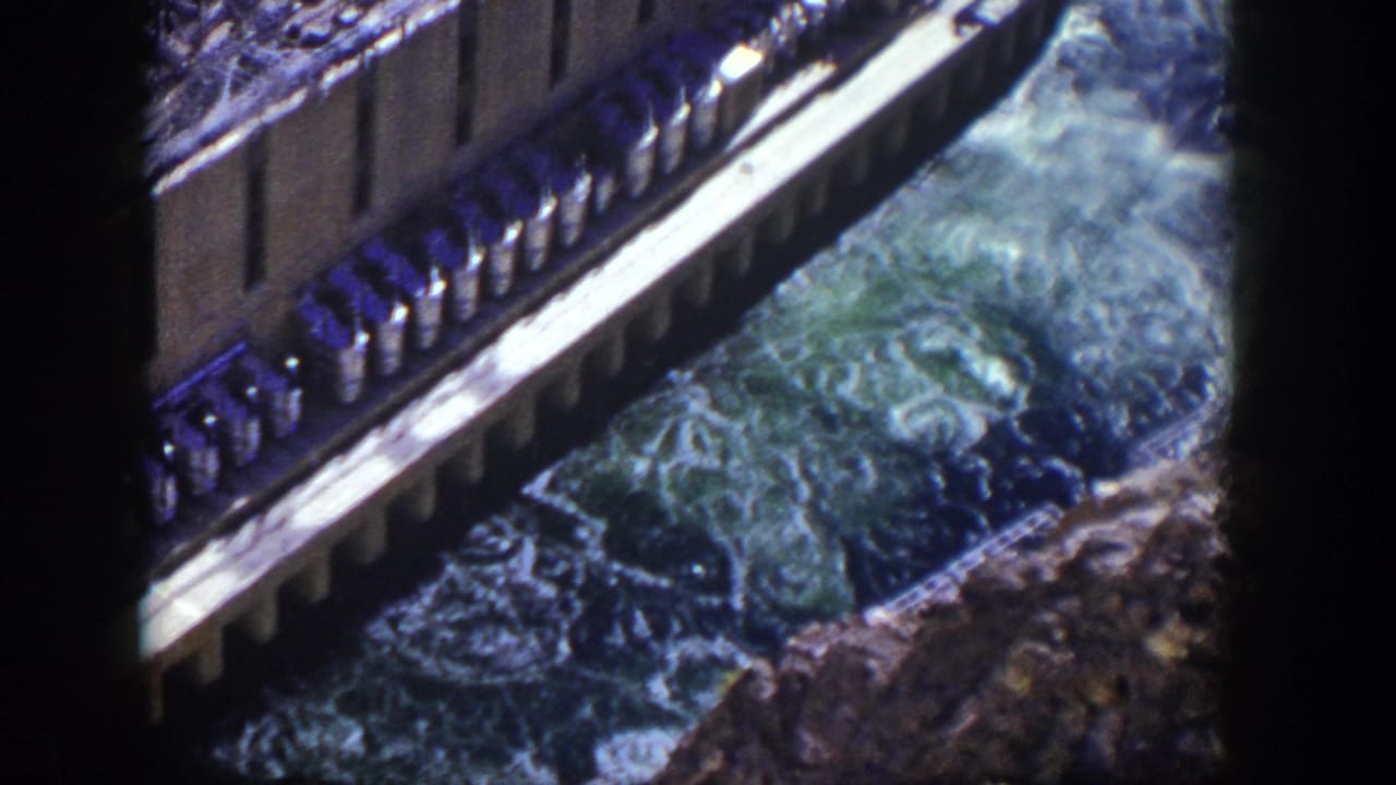 Concrete dam edge and foaming water viewed through dark film borders.