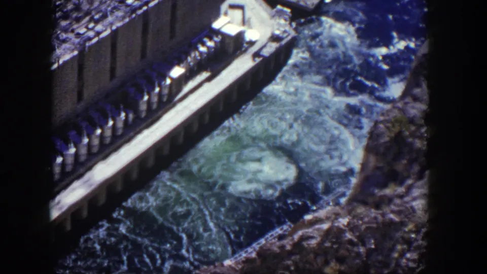1954 Nevada 8mm frame showing a dam edge, bright structural platform, and swirling spillway water below.
