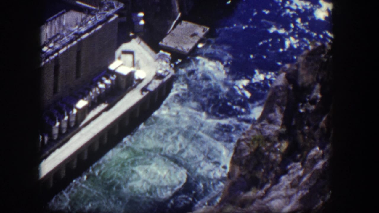 Concrete dam structure beside swirling spillway water and blue reservoir surface.