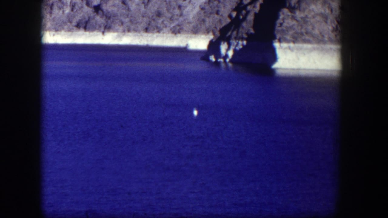 Rocky shoreline and blue water with a bright floating object and dark vertical frame edges.