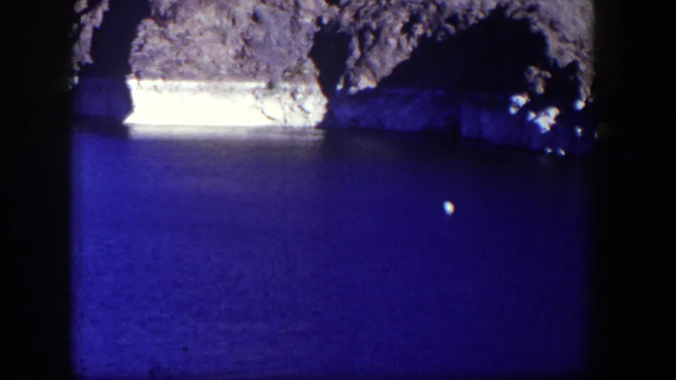 1954 Nevada 8mm frame showing blue water and a rocky shoreline, with heavy gate edges and soft home-movie color.