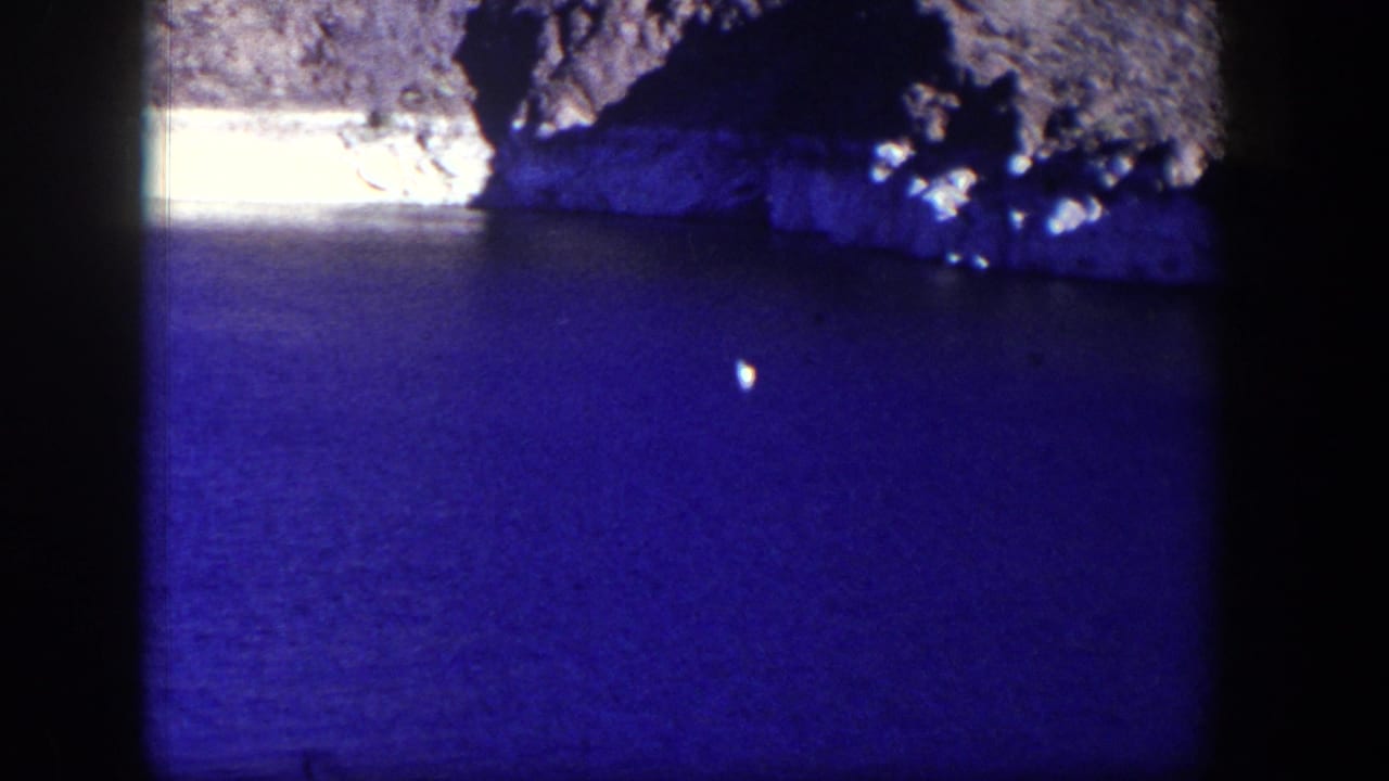 Blue water and rocky shoreline with dark vertical film borders.