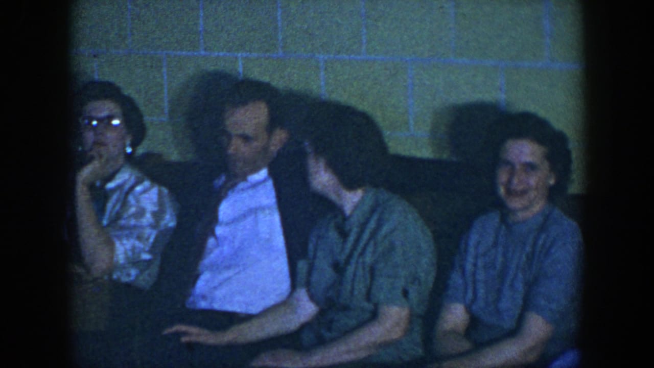 1952 Houston home-movie frame of adults on a couch, with a man in a light shirt seated between two women in a dim private interior.