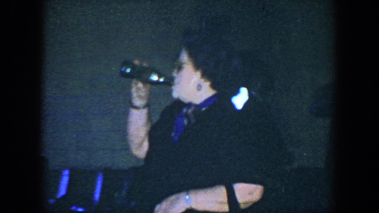 Woman in dark clothing raises a bottle to drink while seated indoors.