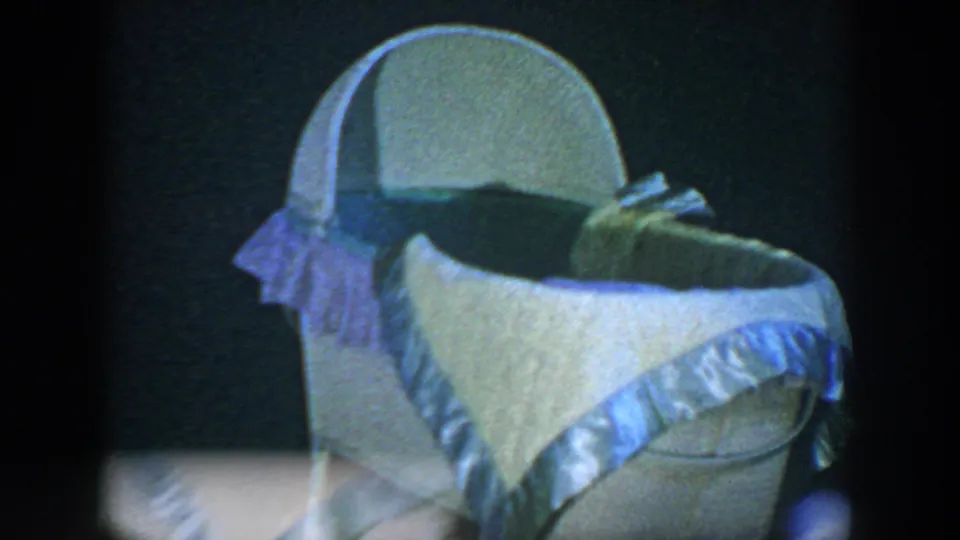 The bassinet fills the frame, showing ruffled trim, an arched hood, and folded bedding in the dim 1952 Houston home-movie scene.