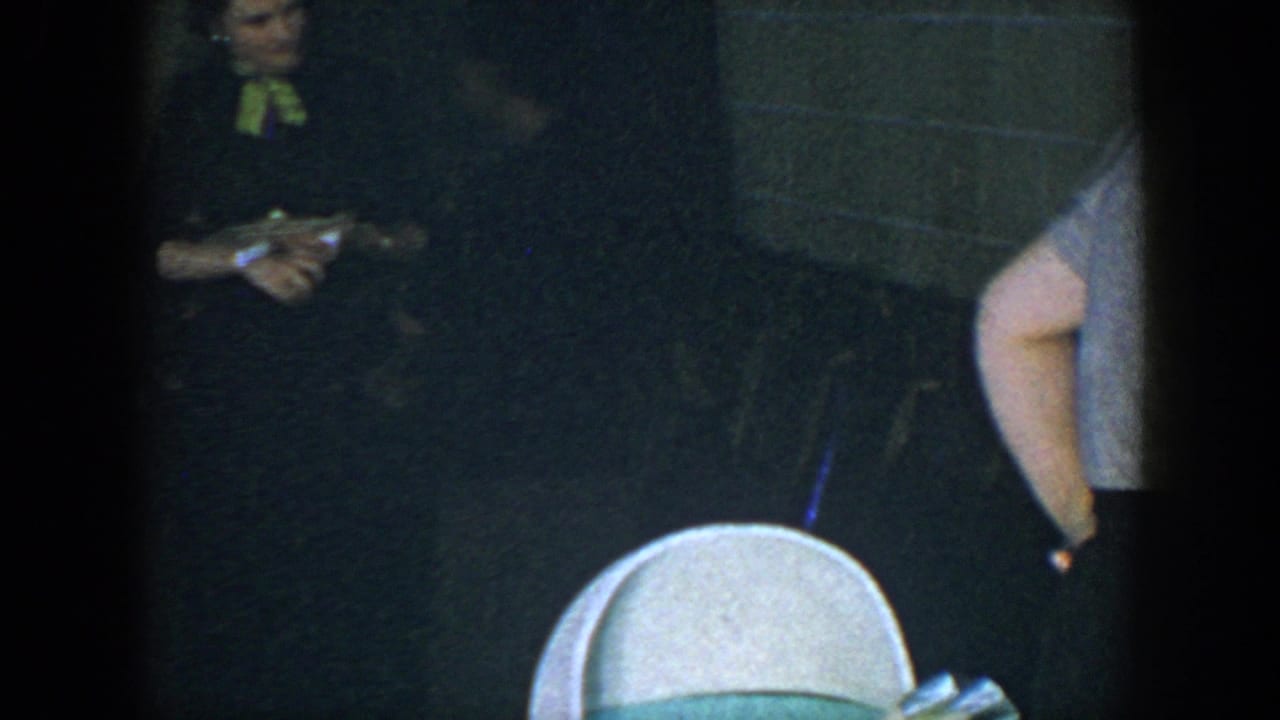 Woman in a dark dress with a bright bow holds an object in a dim room.