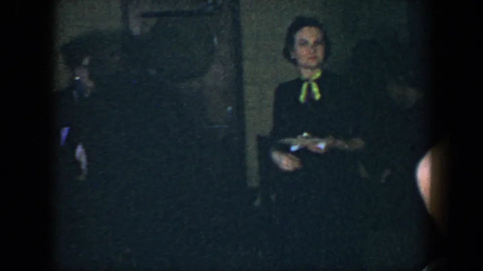 Several adults appear in a dark 1952 Houston interior, including a woman with a bright bow standing near the center of the frame.