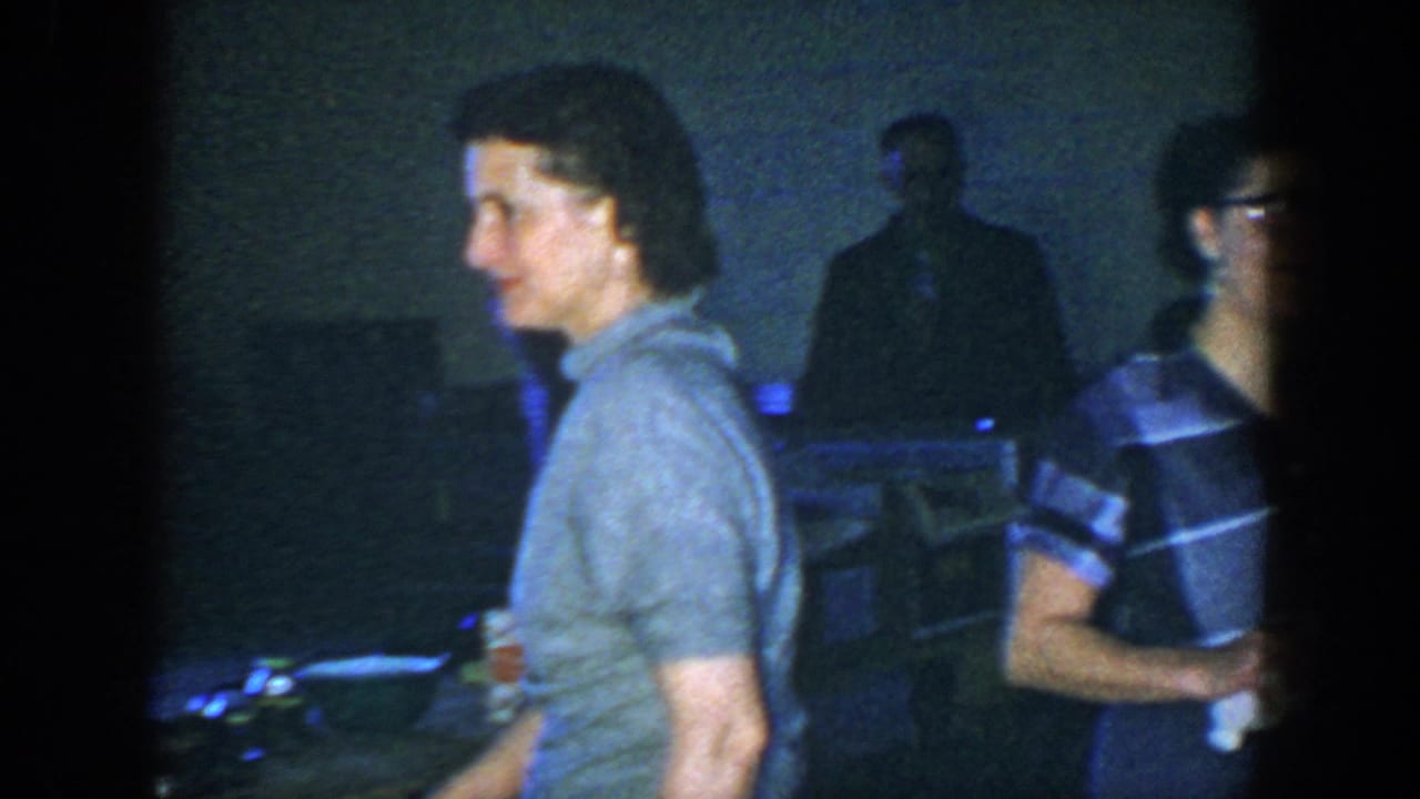 People standing in a dim room near tables with boxes and supplies.