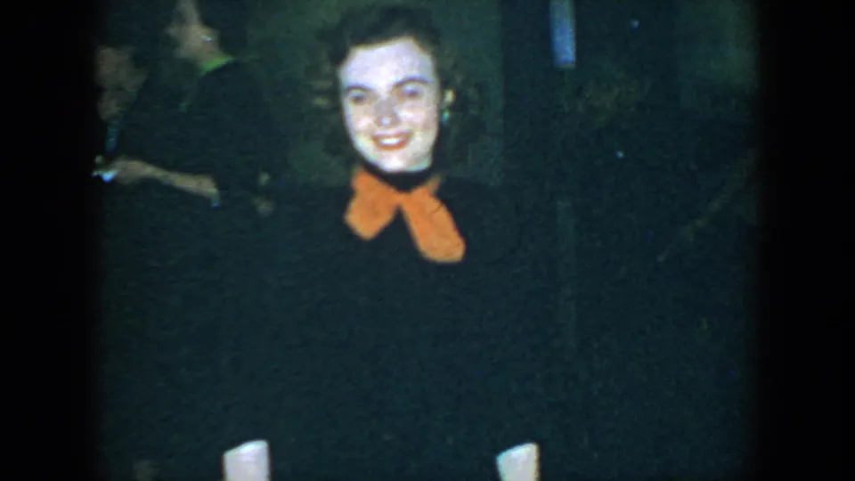 A smiling woman in 1952 Houston home-movie footage is framed close to camera, with shadowed adults nearby.