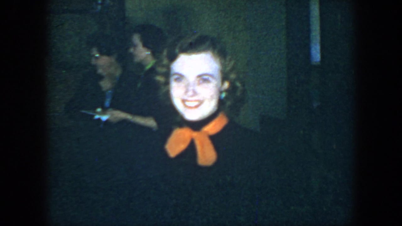 Woman smiles at the camera as background guests stand in the dimly lit room.