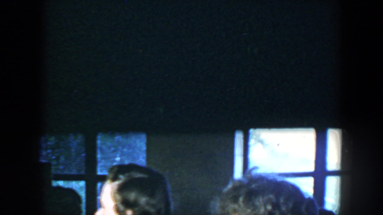 1952 Houston home-movie frame showing a dim room, bright windows, and partially visible adults at an indoor gathering.