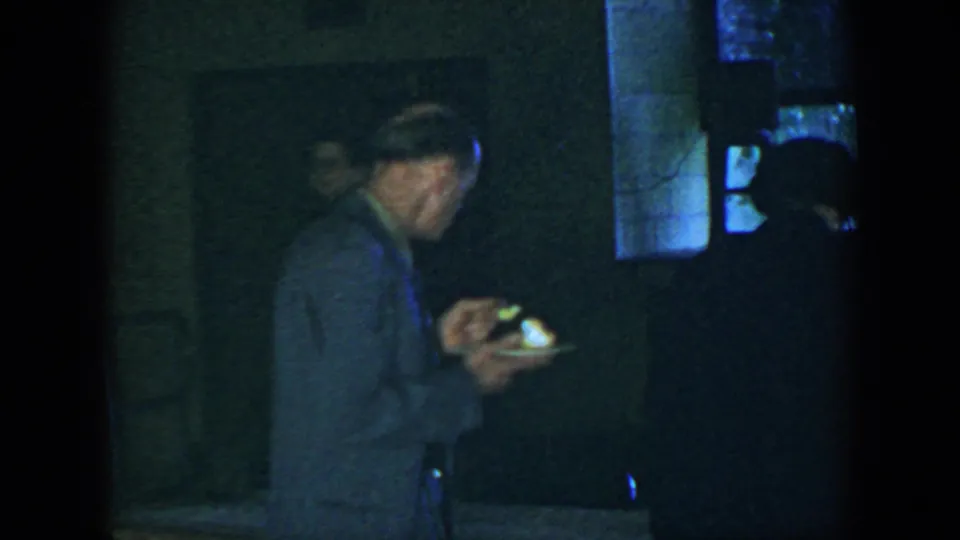 1952 Houston home-movie frame of a suited man holding a small plate while other adults stand in shadow nearby.