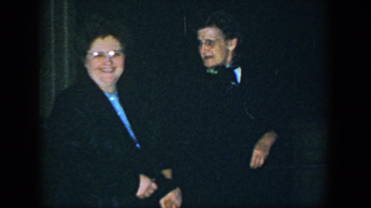 A smiling woman with glasses stands beside a man in a bow tie.