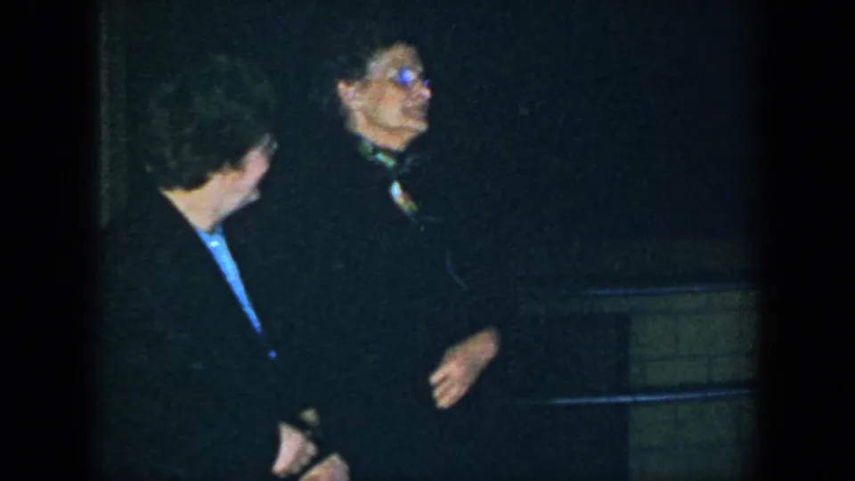 Two adults shift their attention off camera in a dim, grainy 1952 Houston home-movie party scene.