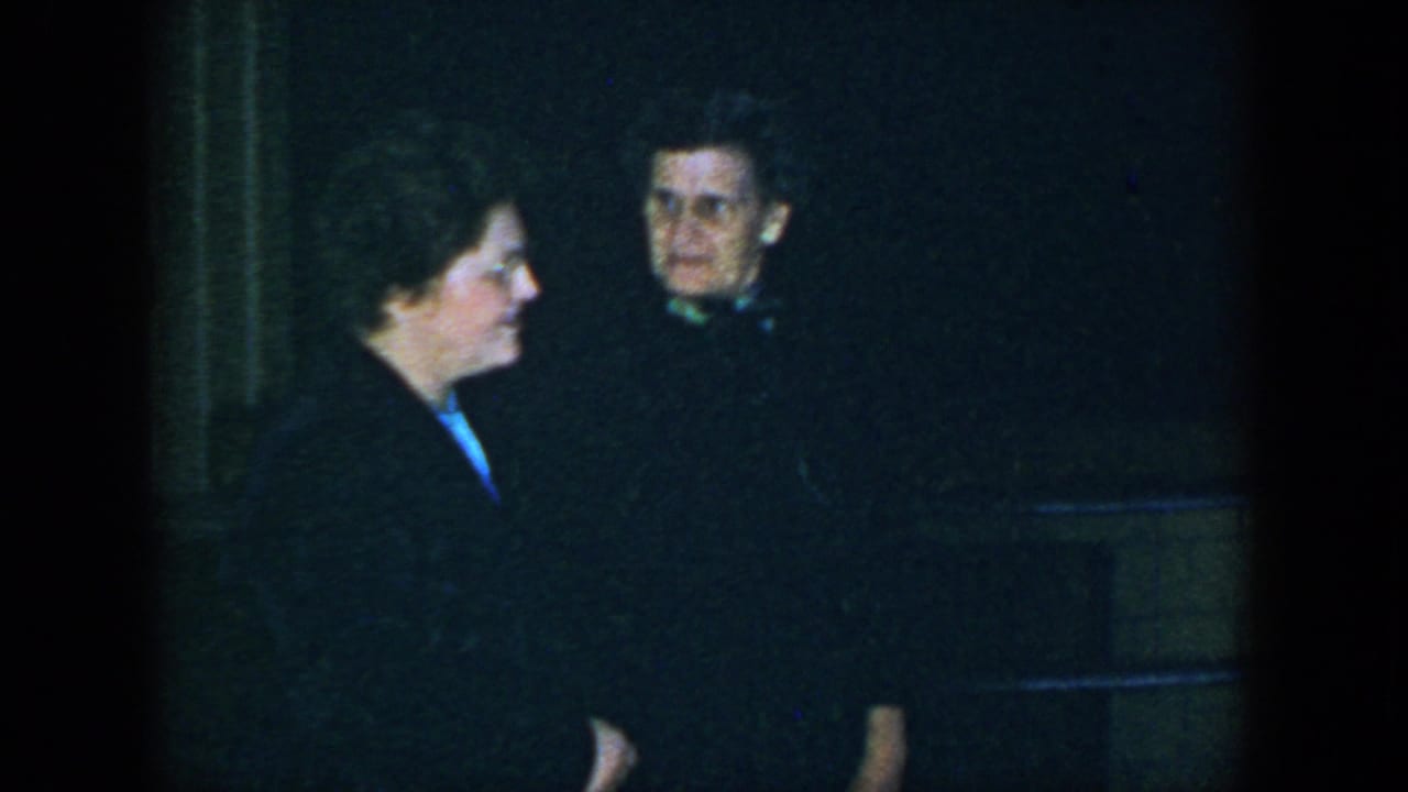 In 1952 Houston footage, one woman in profile faces a glasses-wearing woman in a dark coat.