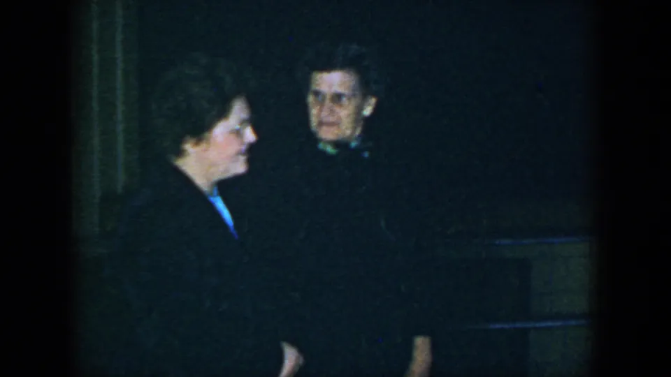 In 1952 Houston footage, one woman in profile faces a glasses-wearing woman in a dark coat.