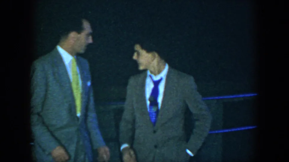 Two suited men converse in a dim interior during the 1952 Houston home-movie social event.