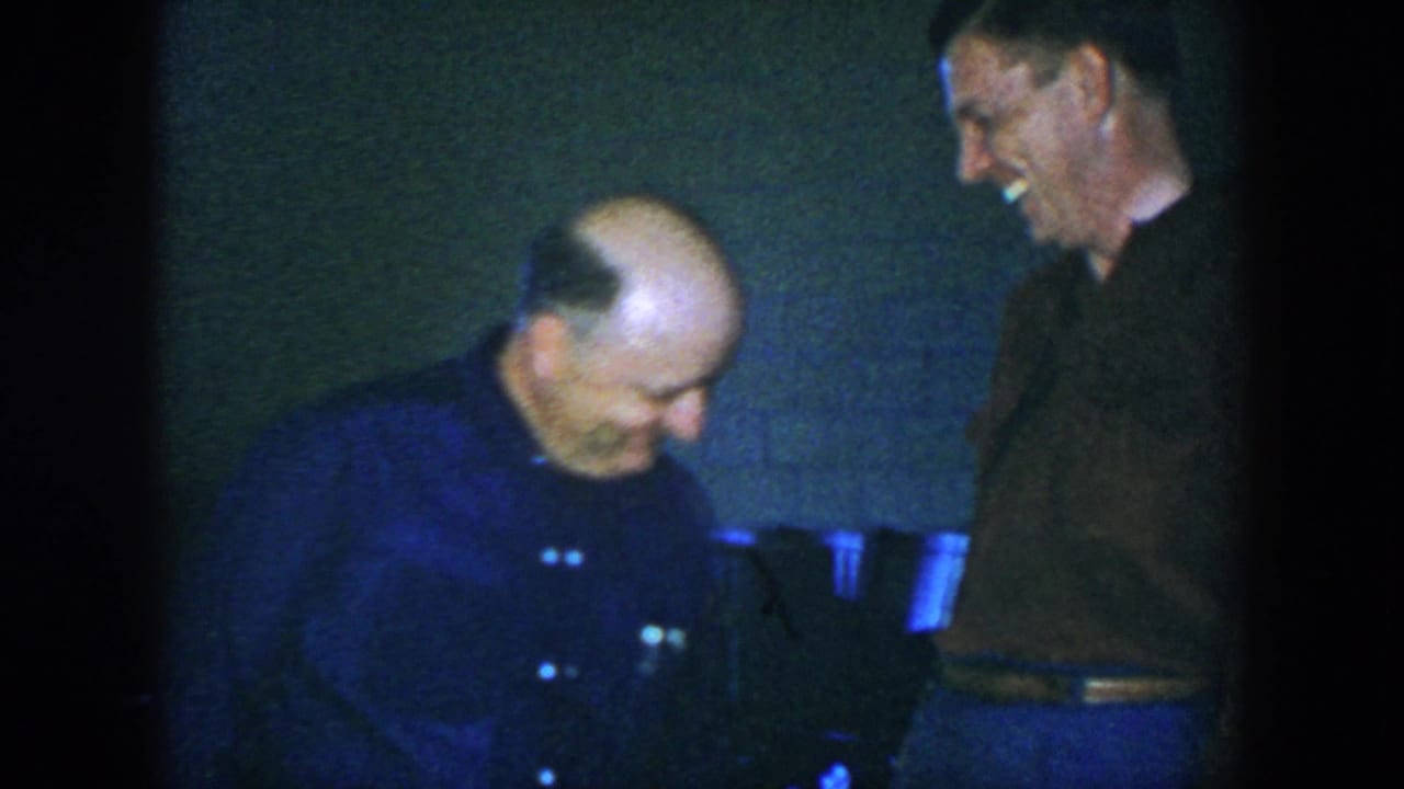 A balding man bends forward laughing while another man smiles beside him.