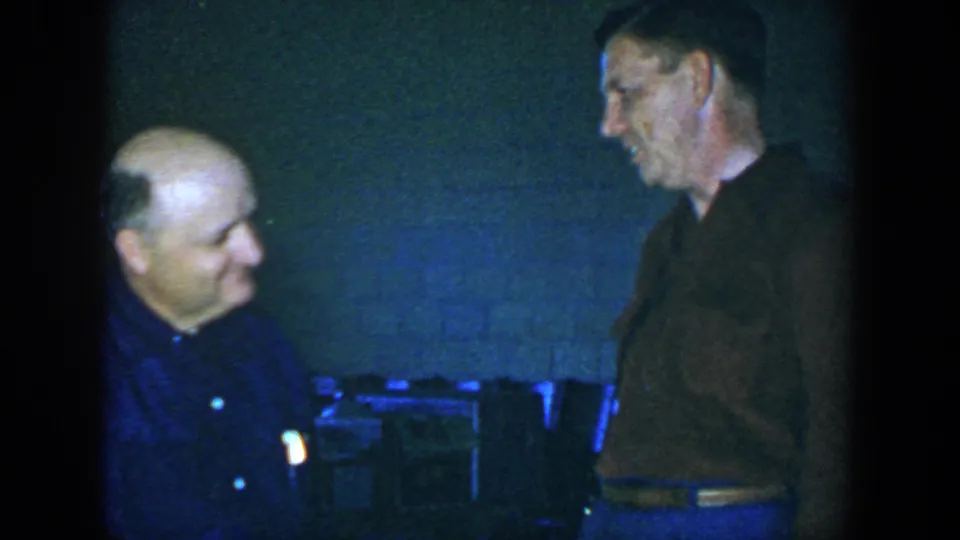 The clip ends with both men smiling in a private indoor Houston setting, captured with soft, grainy 8mm texture.