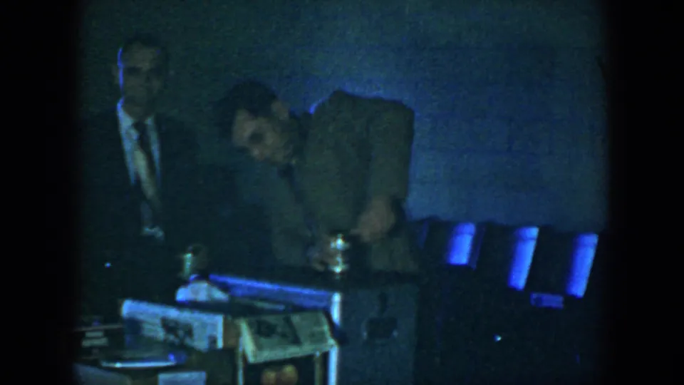 In the final frame, a man bends near a small table or equipment while chairs line the dark interior space.