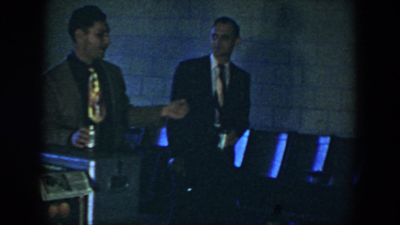 In 1952 Houston home-movie footage, two suited men stand in a dim room near chairs, with one man holding a beer can.