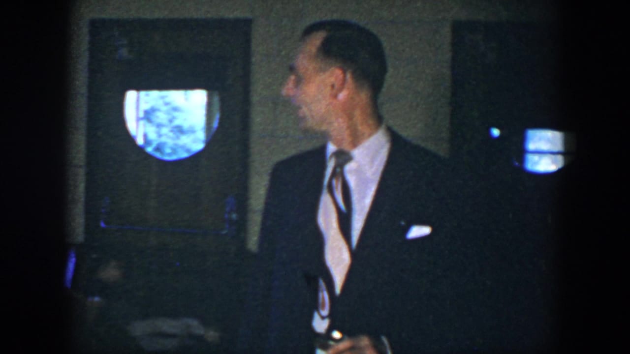 Man in a dark suit looks to the side while holding a drink can indoors.