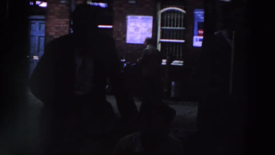 1961 Ireland nighttime exterior with a silhouetted foreground person, blue door, lit notices, and a barred arched doorway.