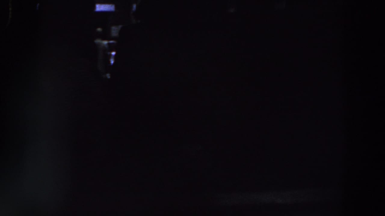 Very dark interior frame with faint lights and indistinct shapes.