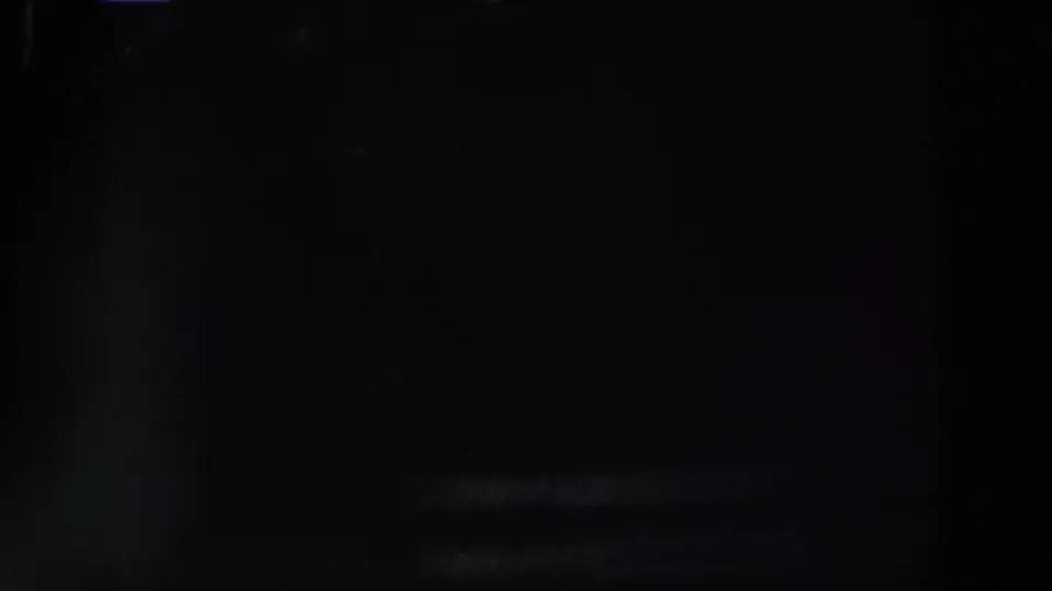 Dark 1961 Ireland home-movie frame with indistinct interior forms and weak light sources in the background.