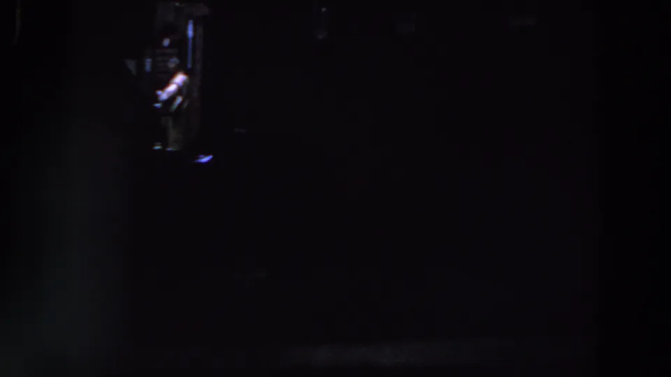 Low-light 8mm frame from Ireland in 1961 with a small bright opening and possible people visible in deep shadow.