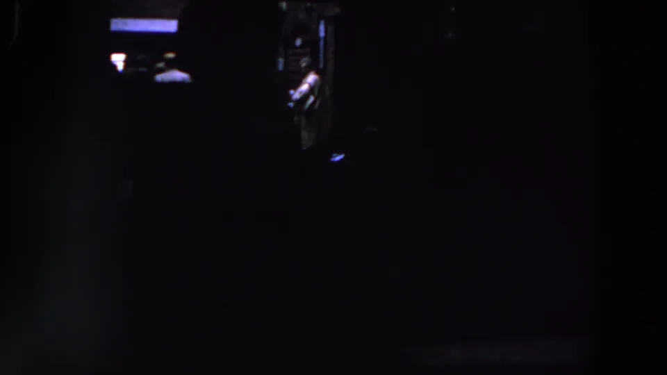 1961 Ireland home-movie frame showing a nearly black room with faint light and an indistinct person or interior feature.