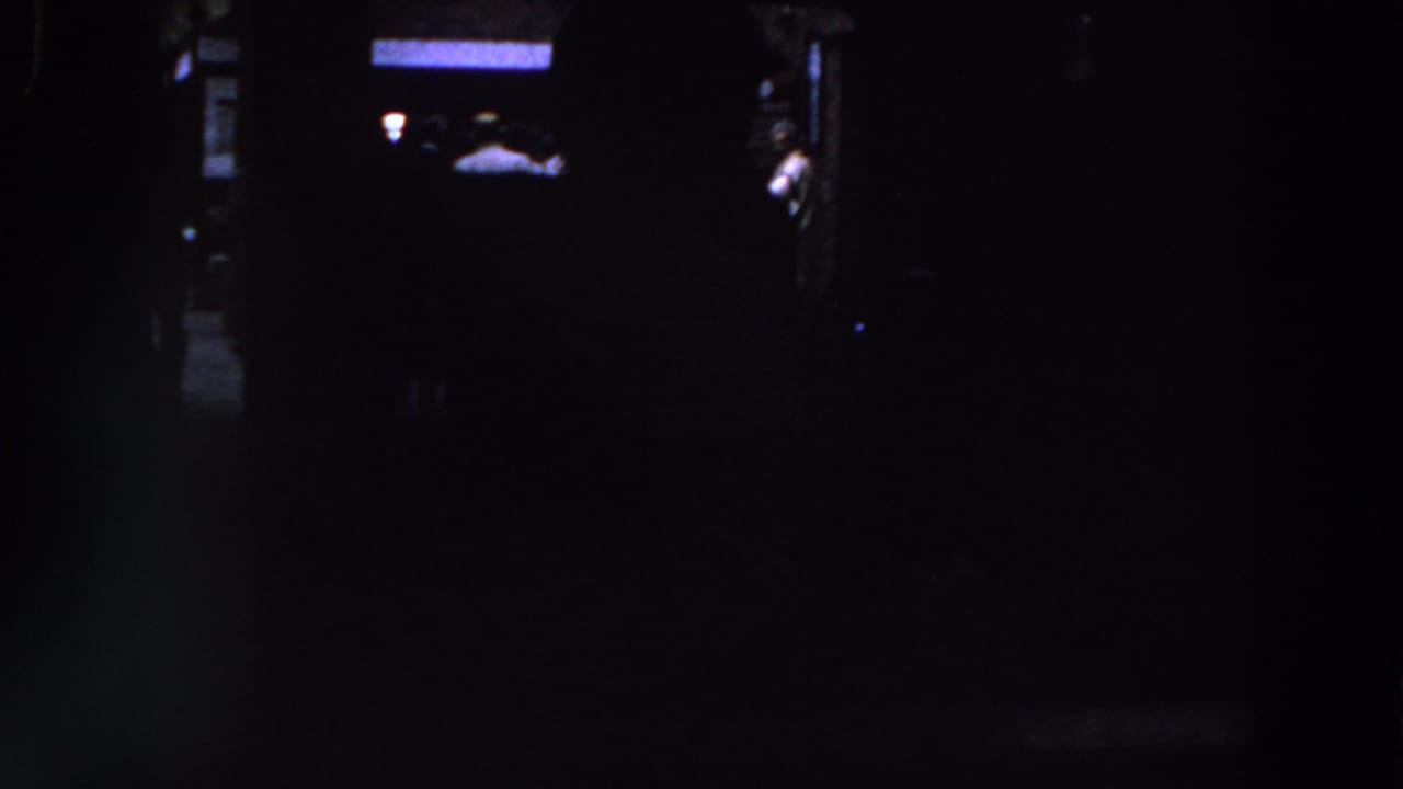 Very dark interior with faint silhouetted figures and small blue-white light patches.