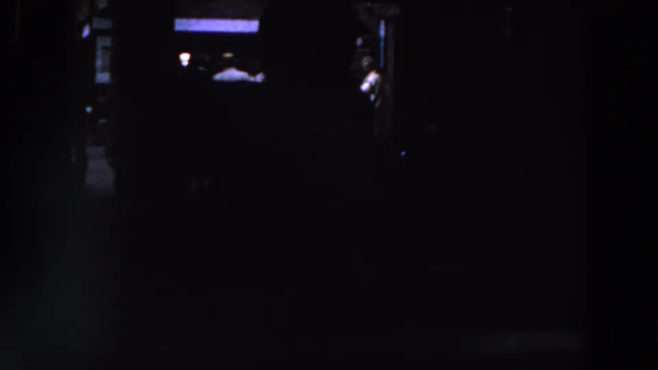 1961 Ireland 8mm frame showing a nearly black indoor scene with indistinct people and small areas of blue-white light.