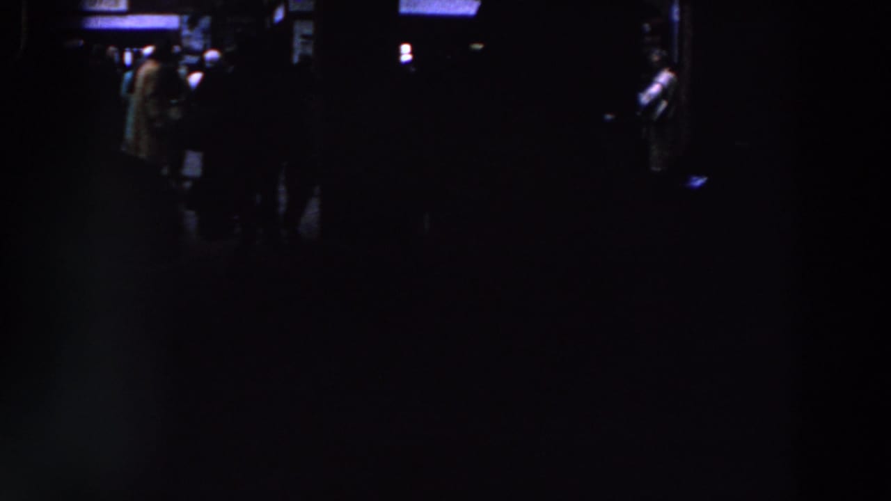 Dark crowded room with faint figures near bright overhead and background light.