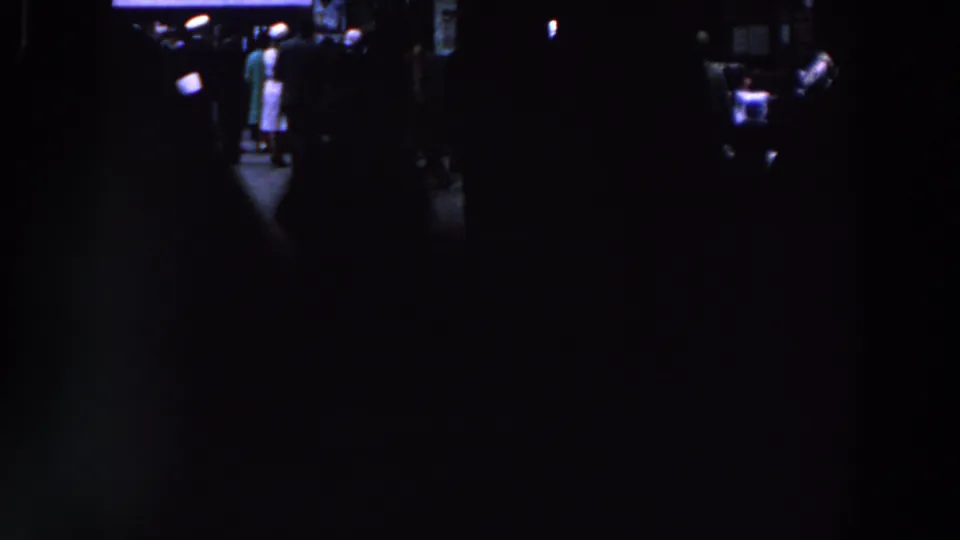 1961 Ireland 8mm frame showing people in silhouette beside a small lit area inside a very dark room.