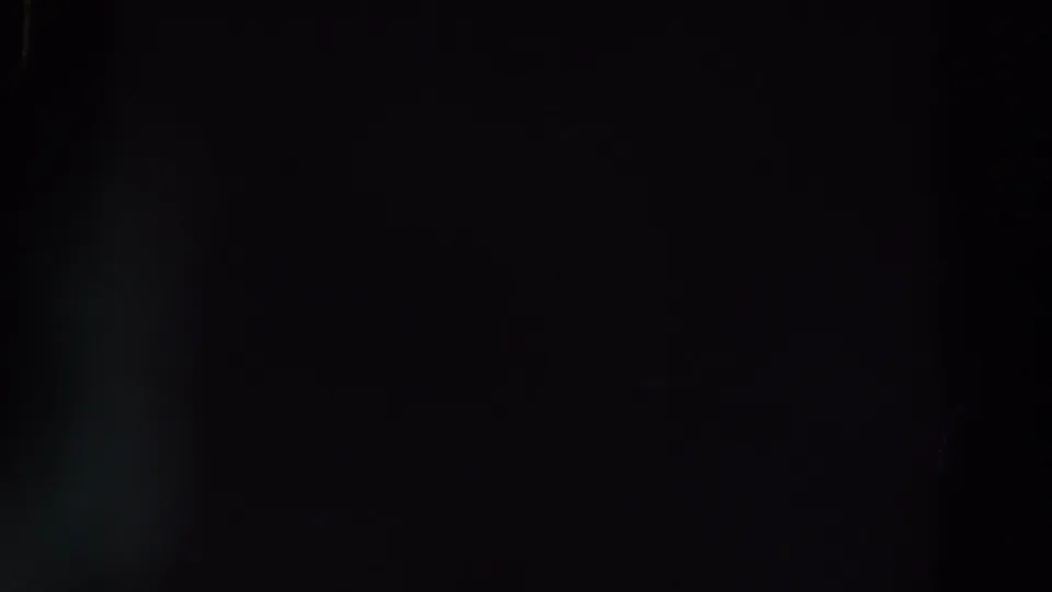 Very dark 8mm frame from the Ireland clip, showing a soft vertical blue-gray glow and indistinct background forms.