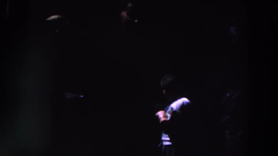 1961 Ireland home-movie frame with a light-shirted person partly illuminated against a nearly black background.