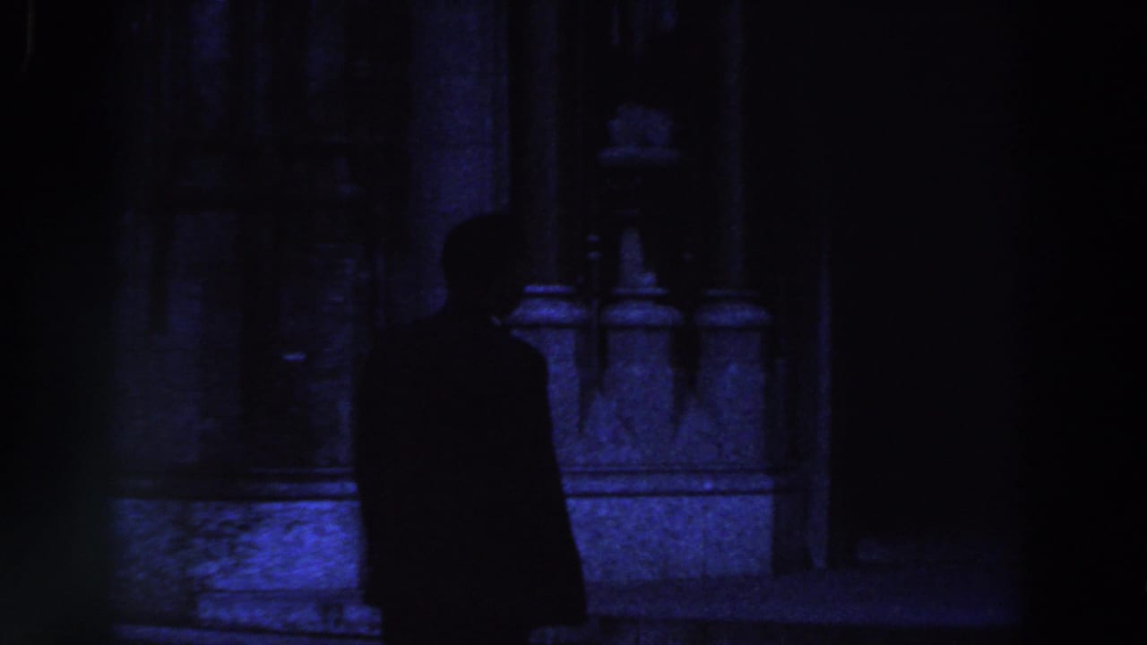 Dark silhouette of a suited man beside a stone building entrance.
