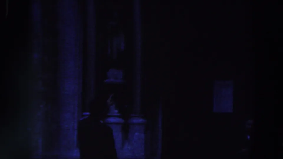 The silhouetted figure moves along the building front, with a dark doorway and posted notice behind him.