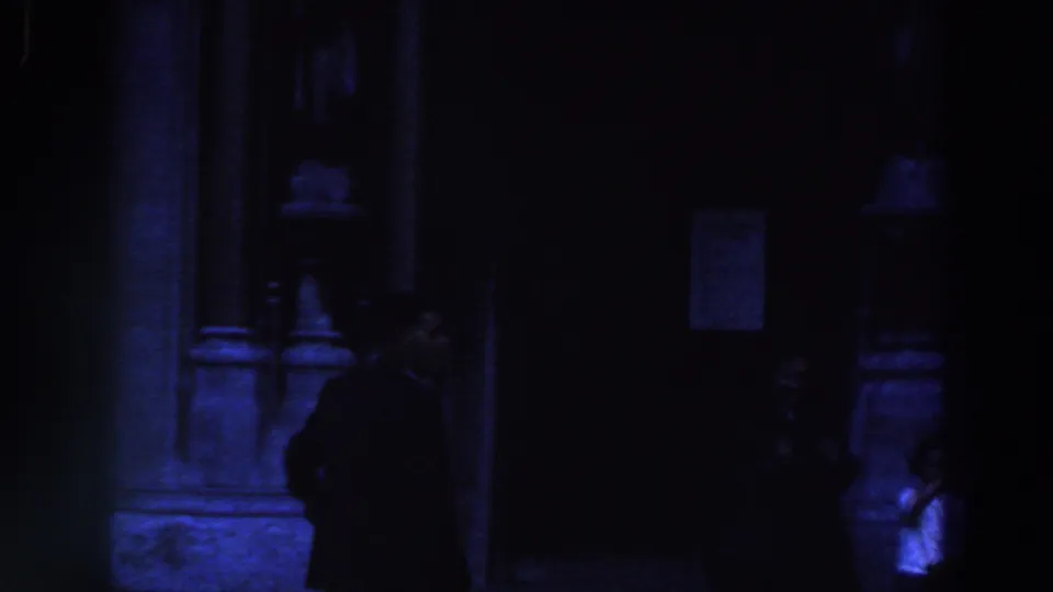 A blue-tinted night exterior shows a suited figure near a doorway, with other people faintly visible at the edge of the frame.